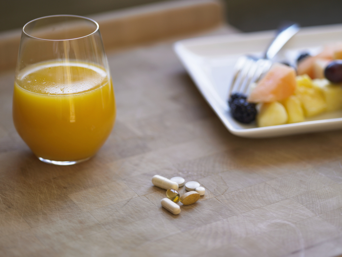 Glass of orange juice, fresh fruit and pills on kitchen counter