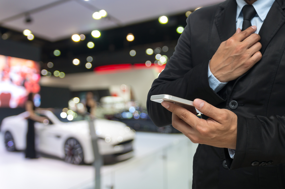 Businessman using the Smart mobile phone on abstract blurred photo of motor show background
